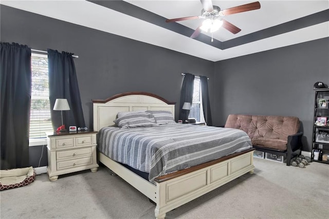 carpeted bedroom with a ceiling fan, a tray ceiling, and baseboards