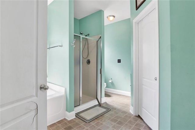 full bathroom with a bath, a shower stall, toilet, and baseboards