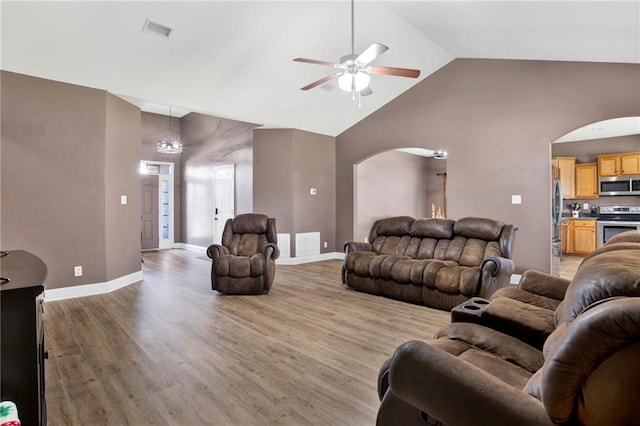 living room featuring baseboards, visible vents, light wood finished floors, arched walkways, and ceiling fan