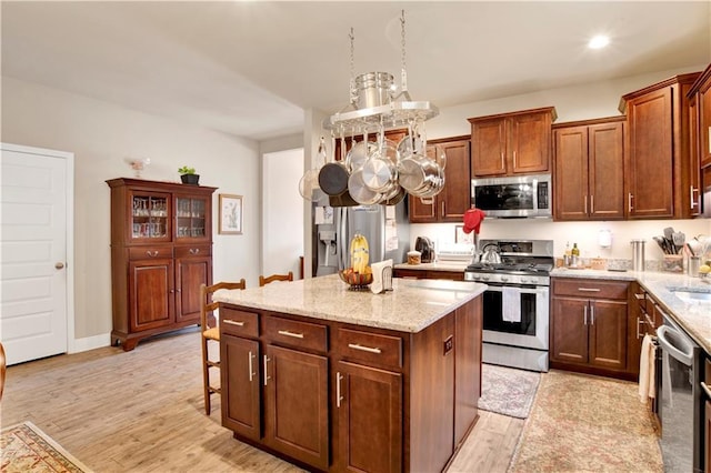 kitchen with sink, stainless steel appliances, a center island, light hardwood / wood-style floors, and light stone countertops