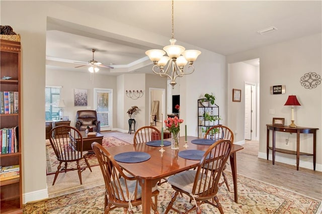 dining area featuring ceiling fan with notable chandelier, a raised ceiling, and light wood-type flooring