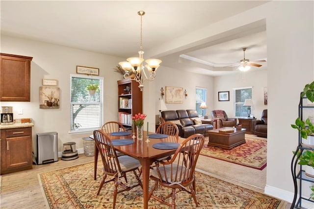 dining space featuring ceiling fan with notable chandelier, a tray ceiling, a wealth of natural light, and light hardwood / wood-style flooring