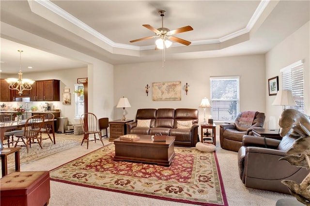 carpeted living room featuring a raised ceiling, ornamental molding, and ceiling fan with notable chandelier