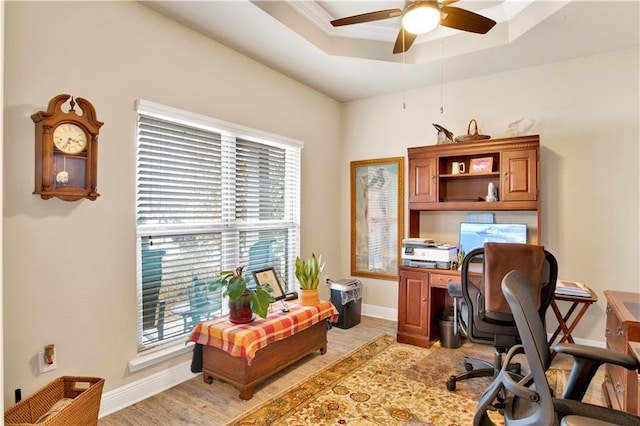 home office featuring a raised ceiling, ceiling fan, a wealth of natural light, and light wood-type flooring