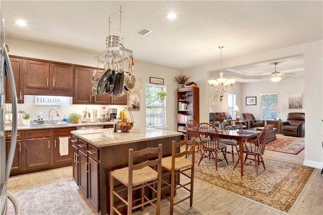 kitchen featuring a kitchen island, pendant lighting, a kitchen bar, light stone countertops, and light hardwood / wood-style flooring