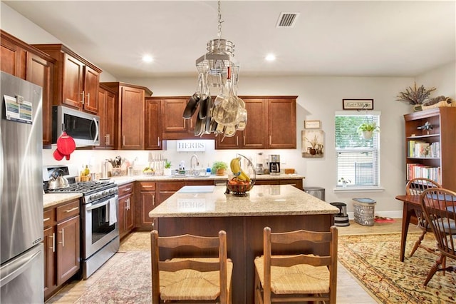 kitchen with a breakfast bar area, appliances with stainless steel finishes, light stone counters, a kitchen island, and decorative light fixtures