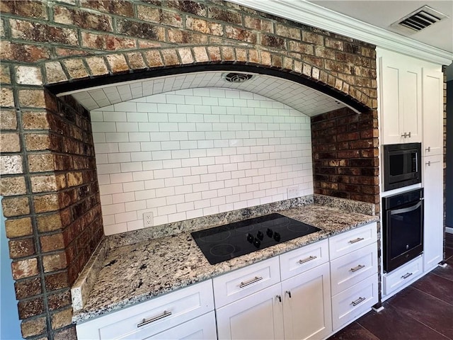 kitchen with light stone counters, white cabinetry, brick wall, and black appliances