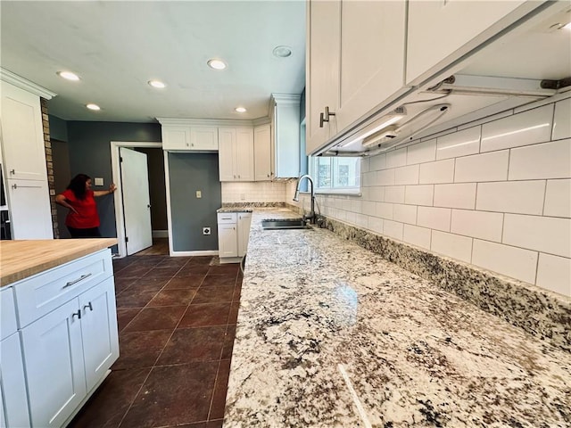 kitchen featuring backsplash, sink, dark tile flooring, and white cabinets