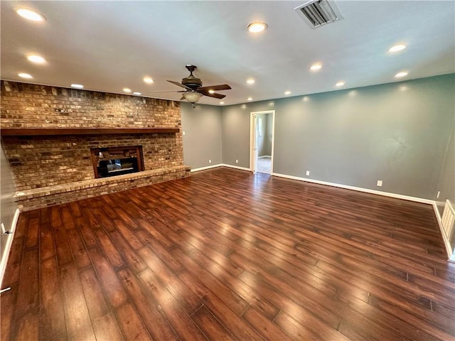 unfurnished living room featuring brick wall, dark wood-type flooring, a brick fireplace, and ceiling fan