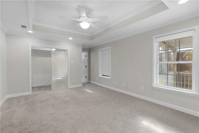 unfurnished bedroom with light colored carpet, visible vents, baseboards, a tray ceiling, and crown molding