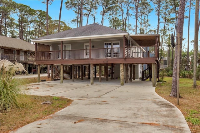 rear view of property featuring a porch, a shingled roof, a carport, driveway, and stairs