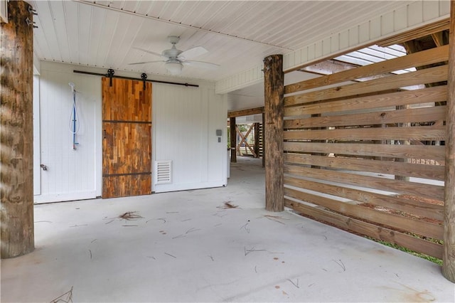 interior space with a barn door, wooden walls, visible vents, ceiling fan, and concrete floors