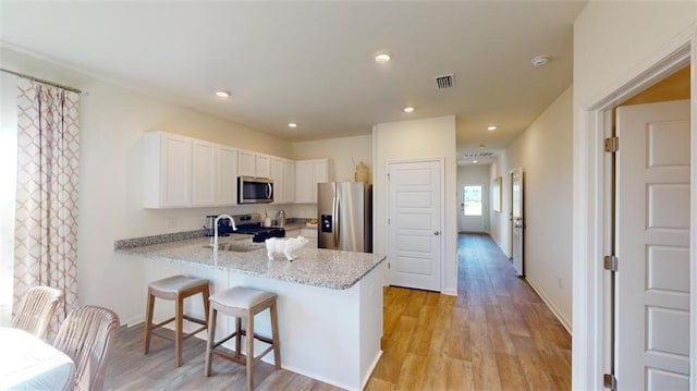 kitchen featuring sink, white cabinetry, appliances with stainless steel finishes, kitchen peninsula, and light stone countertops