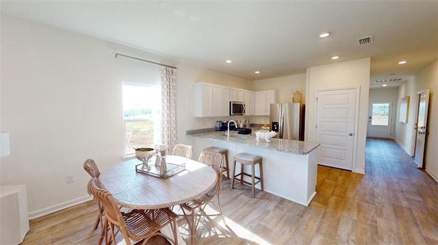 kitchen with appliances with stainless steel finishes, white cabinetry, light stone counters, kitchen peninsula, and light wood-type flooring