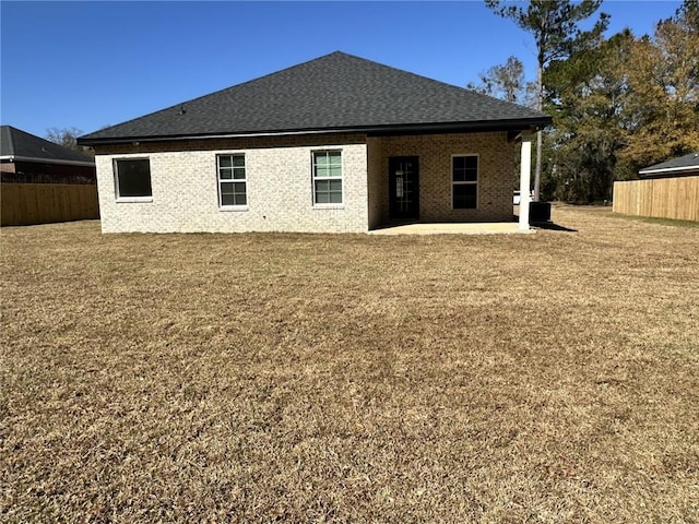 rear view of house with a patio, brick siding, a shingled roof, fence, and a lawn