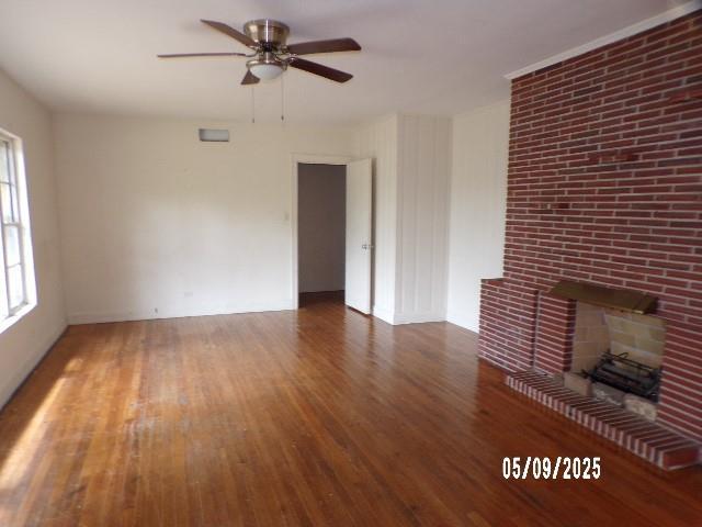 unfurnished living room featuring a ceiling fan, wood finished floors, and a fireplace