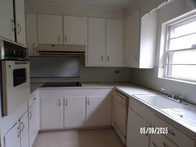 kitchen featuring white appliances, under cabinet range hood, white cabinetry, light countertops, and crown molding