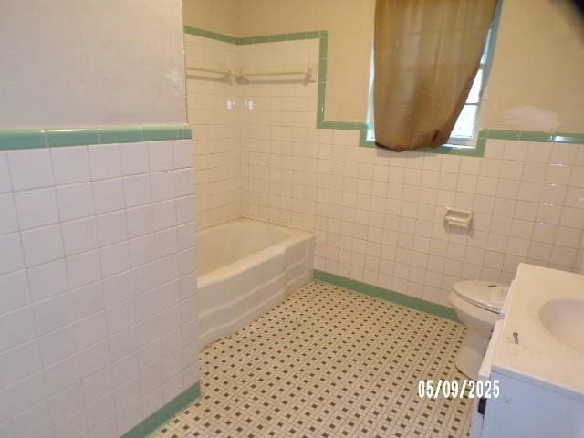 full bath with tile walls, wainscoting, vanity, toilet, and shower / bath combination