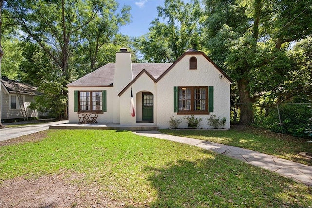 tudor-style house featuring stucco siding, a front yard, a chimney, and fence