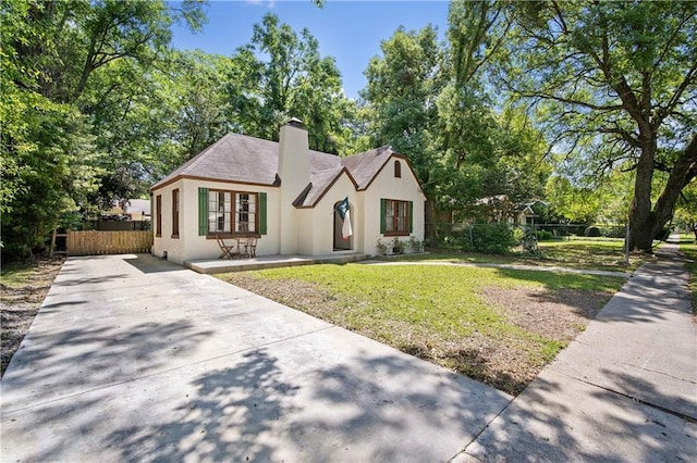 tudor home featuring a chimney, fence, stucco siding, concrete driveway, and a front yard