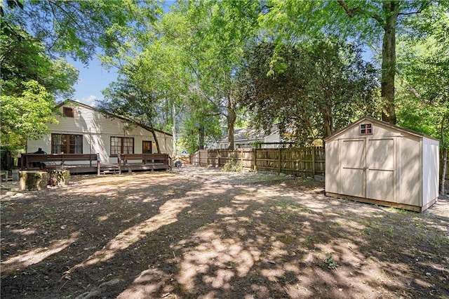 view of yard with fence, a wooden deck, a storage unit, and an outbuilding