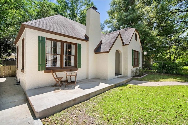 view of front facade featuring stucco siding, a front yard, a chimney, and fence
