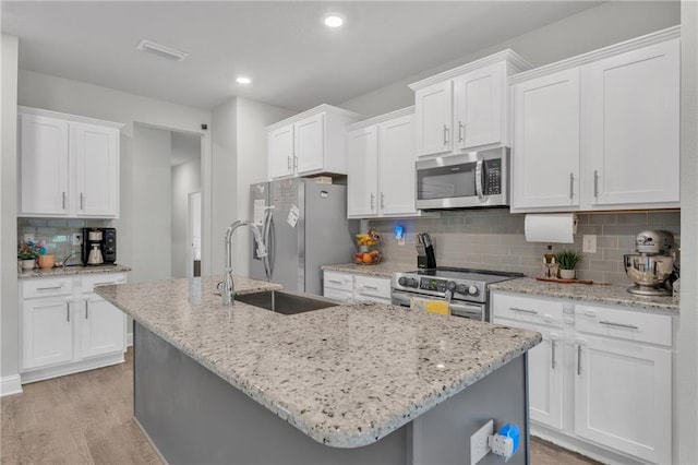 kitchen featuring stainless steel appliances, a kitchen island with sink, white cabinetry, light wood-type flooring, and tasteful backsplash