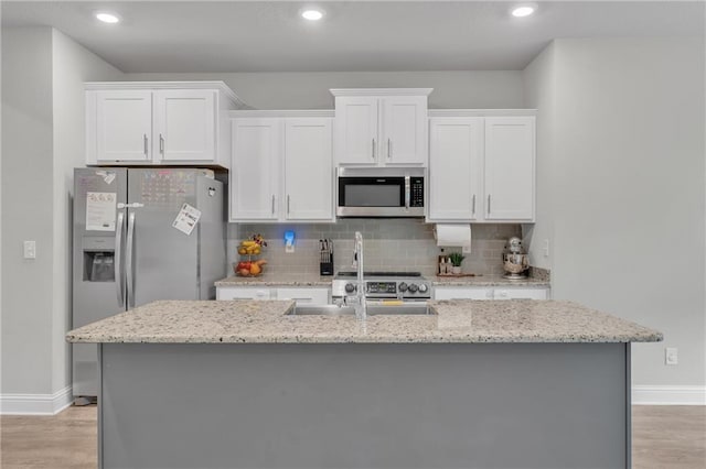 kitchen with appliances with stainless steel finishes, baseboards, white cabinetry, light wood-style floors, and an island with sink