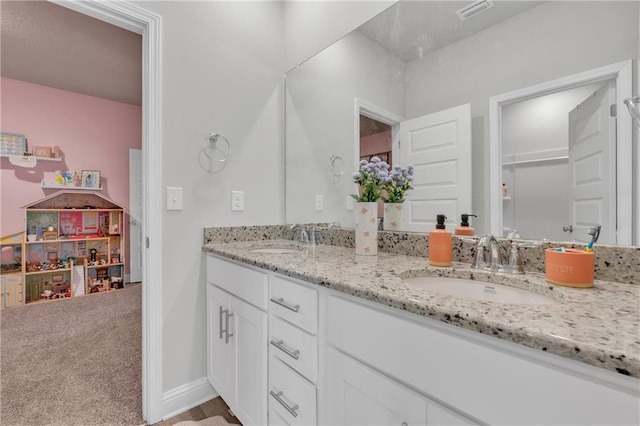 bathroom with a sink, double vanity, baseboards, and visible vents