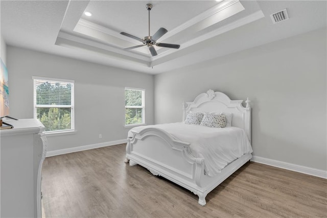 bedroom with crown molding, a tray ceiling, visible vents, and wood finished floors