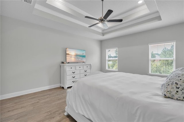 bedroom featuring crown molding, light wood-style flooring, ceiling fan, a tray ceiling, and baseboards