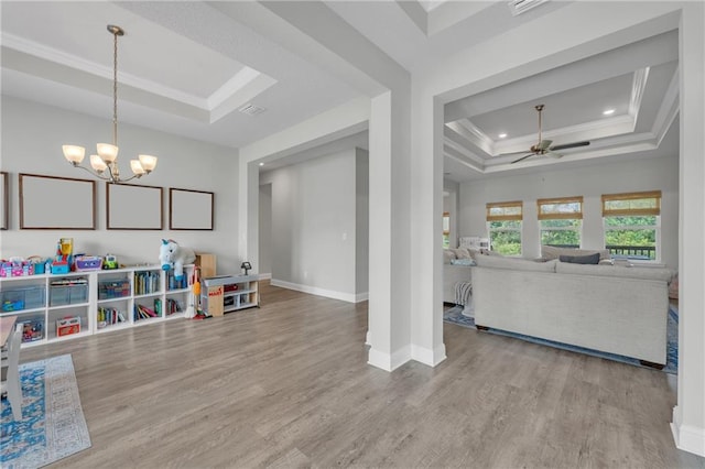 rec room featuring wood finished floors, ceiling fan with notable chandelier, a tray ceiling, baseboards, and ornamental molding