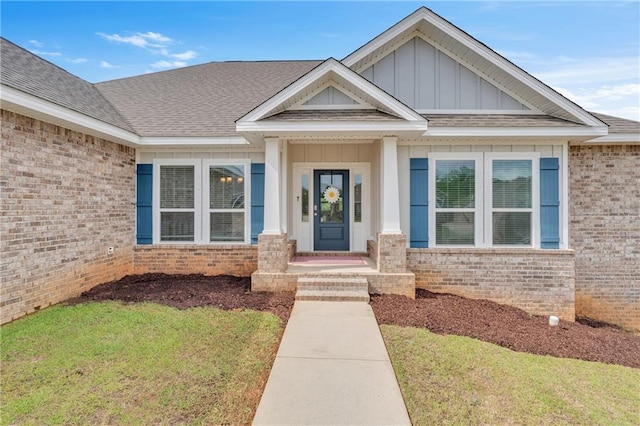 property entrance featuring a lawn, board and batten siding, brick siding, and a shingled roof
