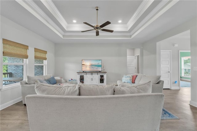 living area with a tray ceiling, ceiling fan, baseboards, and plenty of natural light