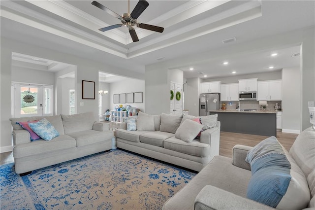 living room with a ceiling fan, light wood-type flooring, a raised ceiling, and recessed lighting