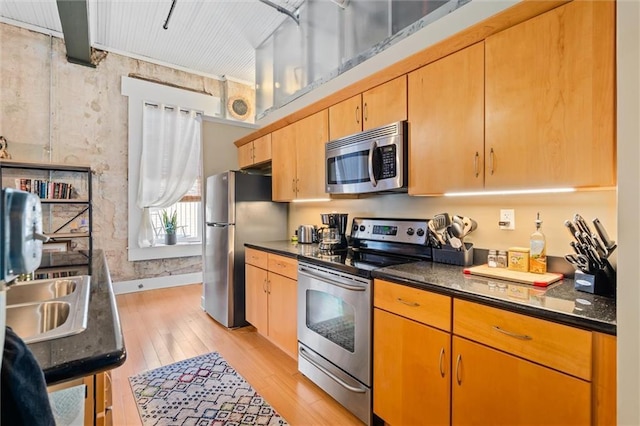 kitchen with stainless steel appliances, sink, light hardwood / wood-style flooring, and dark stone counters