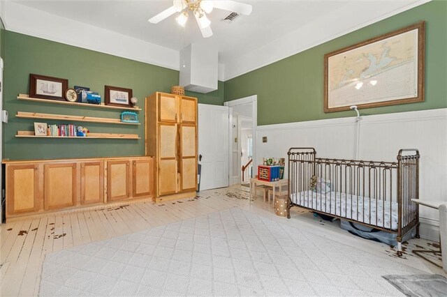 206 George St, Mobile, AL 36604 - bedroom featuring light wood-style floors, wainscoting, a crib, and ceiling fan