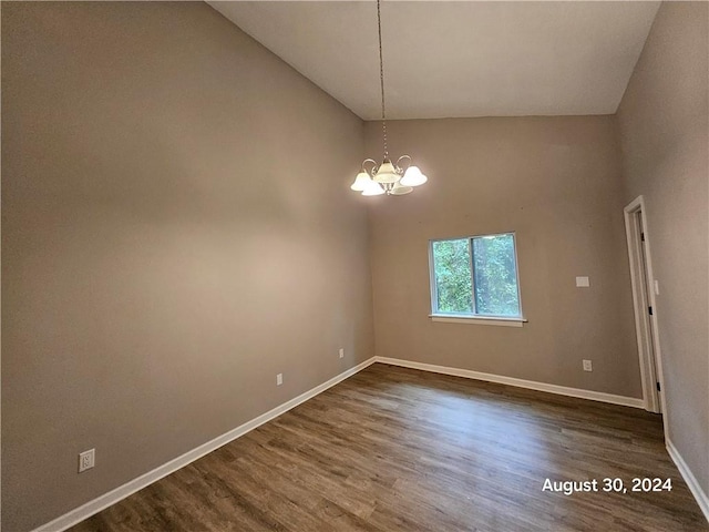 empty room with dark wood-type flooring, high vaulted ceiling, and a notable chandelier