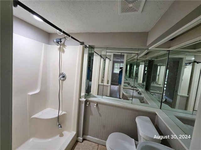 bathroom featuring a textured ceiling, toilet, and walk in shower