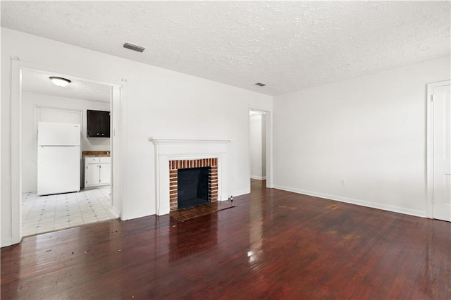 unfurnished living room with hardwood / wood-style floors, a textured ceiling, and a brick fireplace