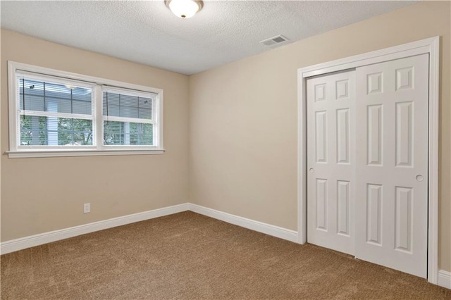 unfurnished bedroom with a textured ceiling, carpet floors, and a closet