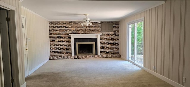 unfurnished living room featuring wooden walls, a fireplace, carpet floors, ceiling fan, and crown molding