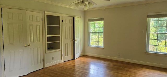 unfurnished bedroom featuring hardwood / wood-style floors, two closets, ornamental molding, and ceiling fan