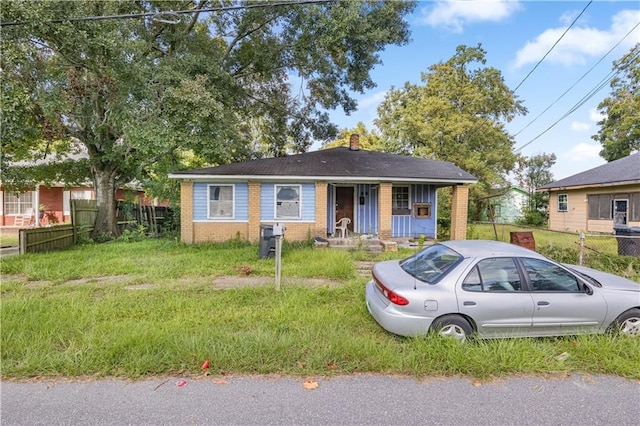 bungalow featuring brick siding, fence, a chimney, and a front lawn