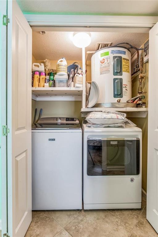 washroom with water heater, light tile patterned floors, washer and dryer, and a textured ceiling