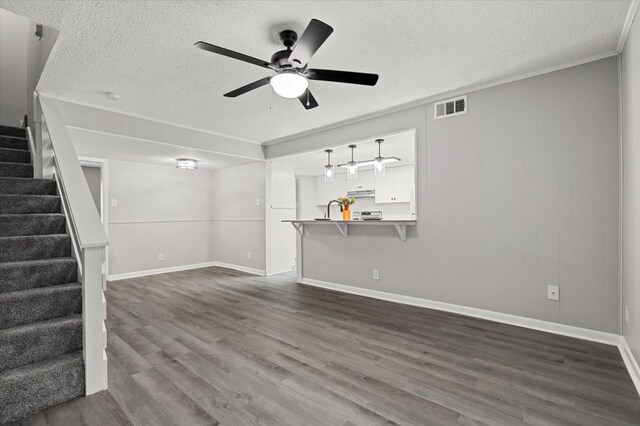 unfurnished living room featuring sink, crown molding, dark hardwood / wood-style floors, ceiling fan, and a textured ceiling