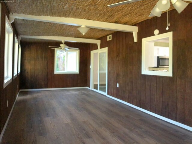 empty room featuring wood walls, beam ceiling, and dark wood-type flooring