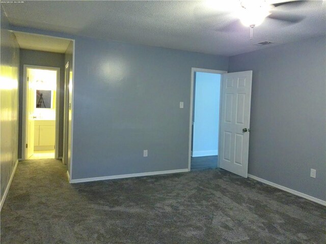 spare room with a textured ceiling, dark carpet, and ceiling fan