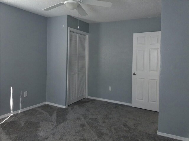 unfurnished bedroom featuring dark colored carpet, a textured ceiling, a closet, and ceiling fan