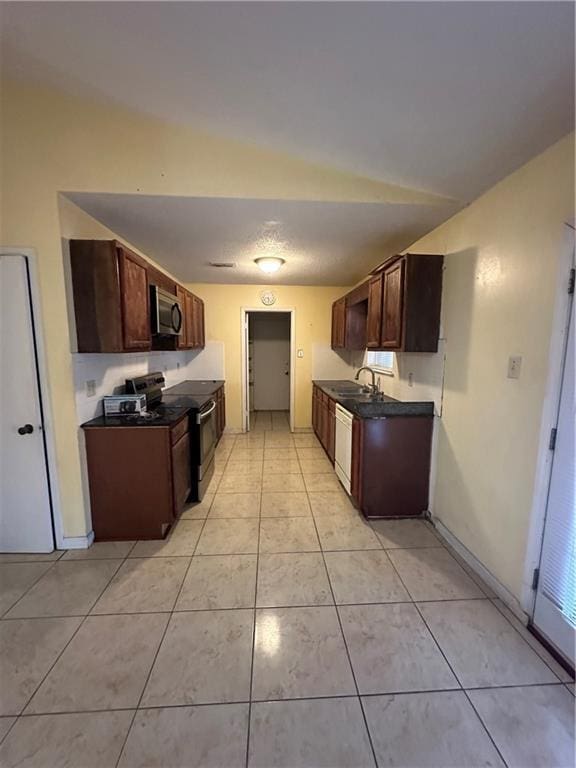 kitchen featuring black electric range, dark countertops, stainless steel microwave, light tile patterned flooring, and white dishwasher